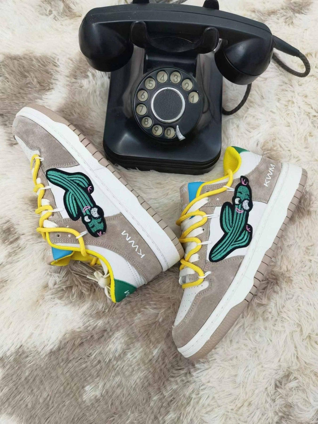 TALISHKO board shoes with cactus motif and yellow laces beside vintage rotary phone on carpet.