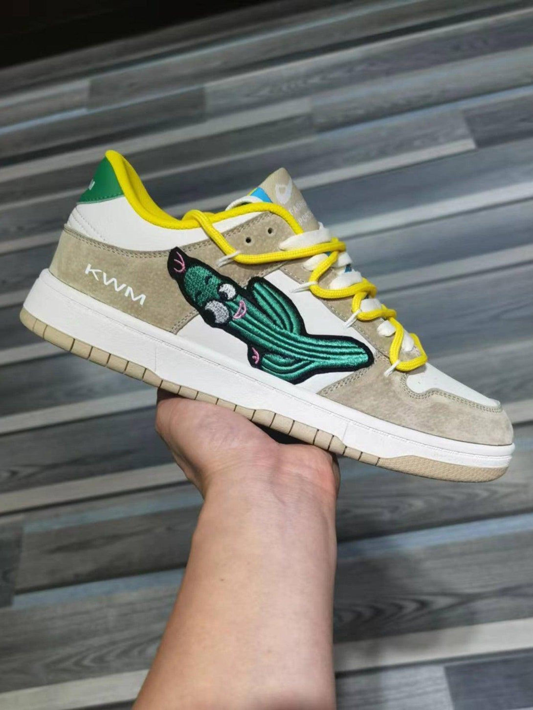 Side view of TALISHKO board shoes with cactus design and yellow laces, held in hand.