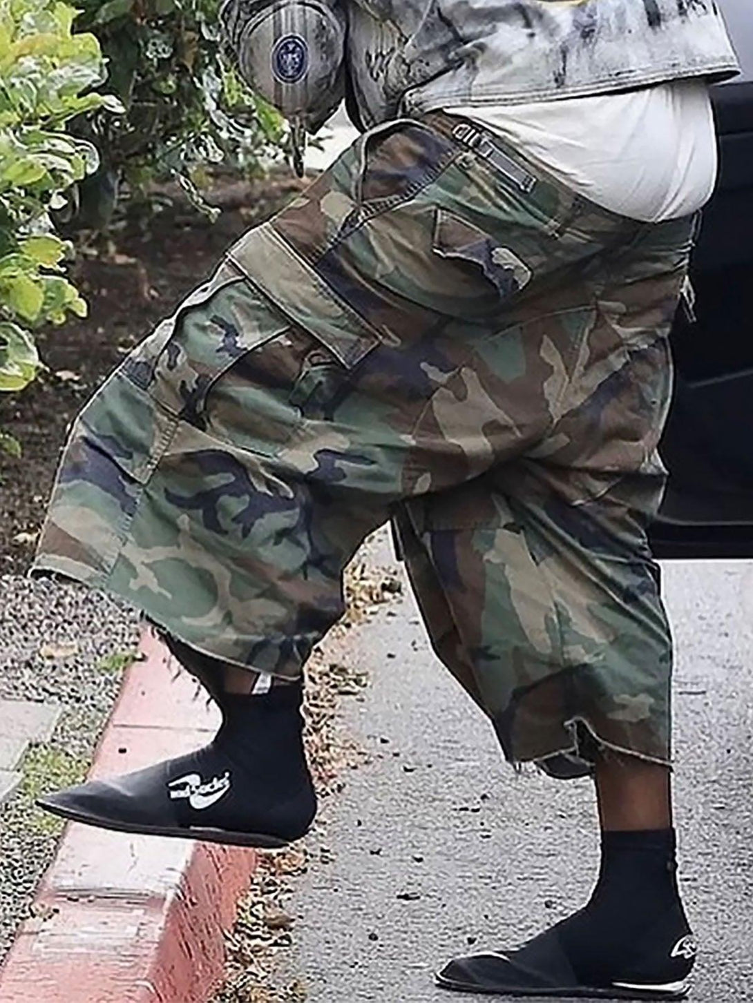 TALISHKO camouflage cropped cargo shorts with buckle waist, worn casually with unique footwear.