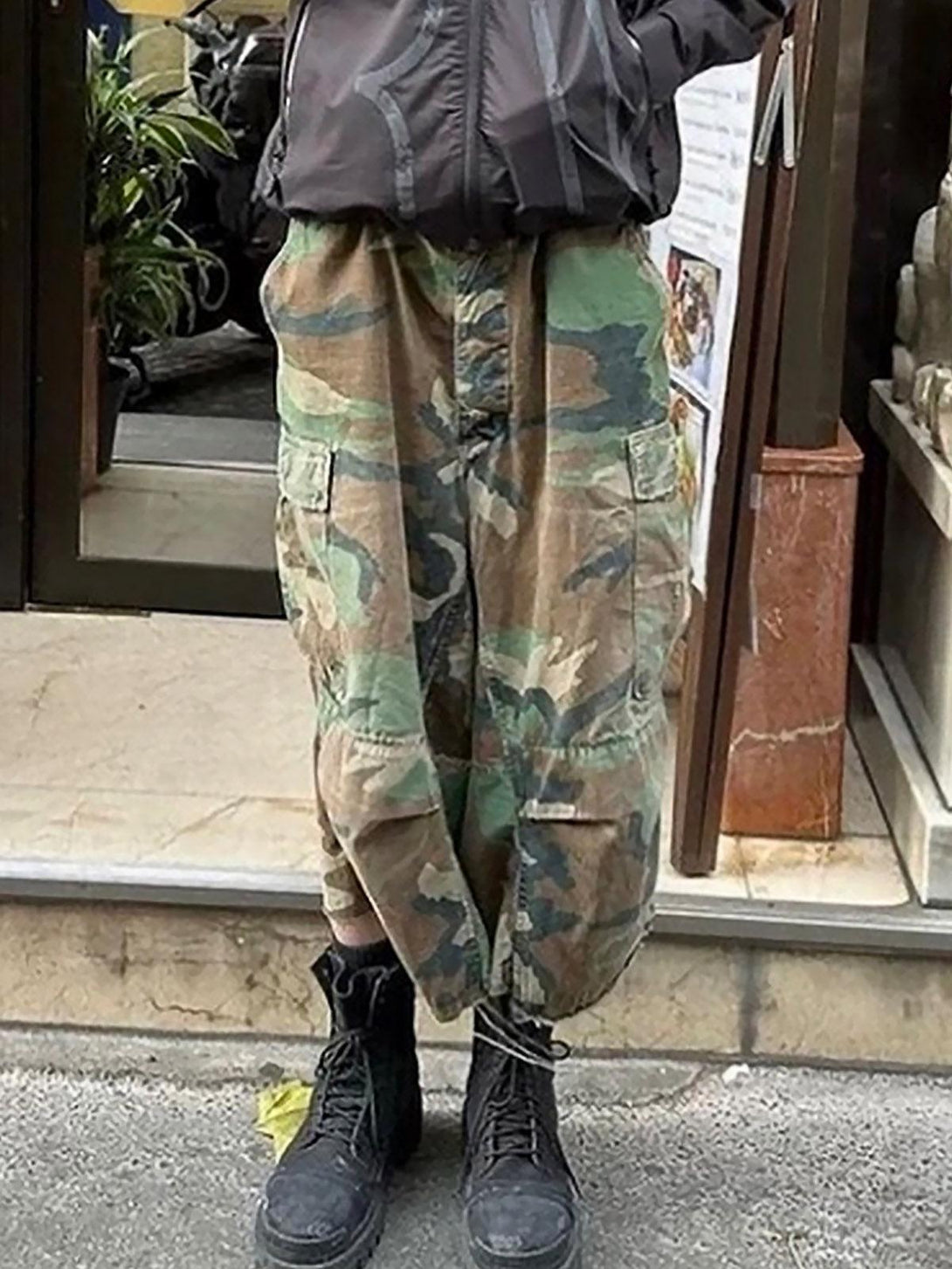Person wearing TALISHKO camouflage cropped cargo shorts with buckle waist and black boots.