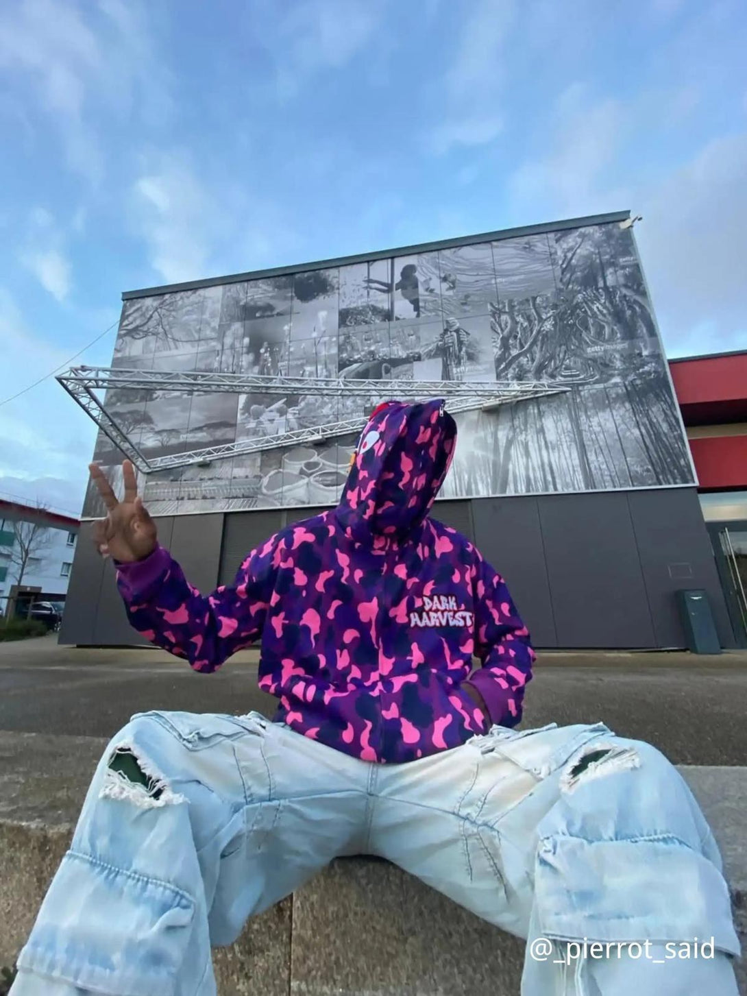 Model wearing a vibrant camouflage hoodie with double cap design by TALISHKO, paired with distressed jeans.