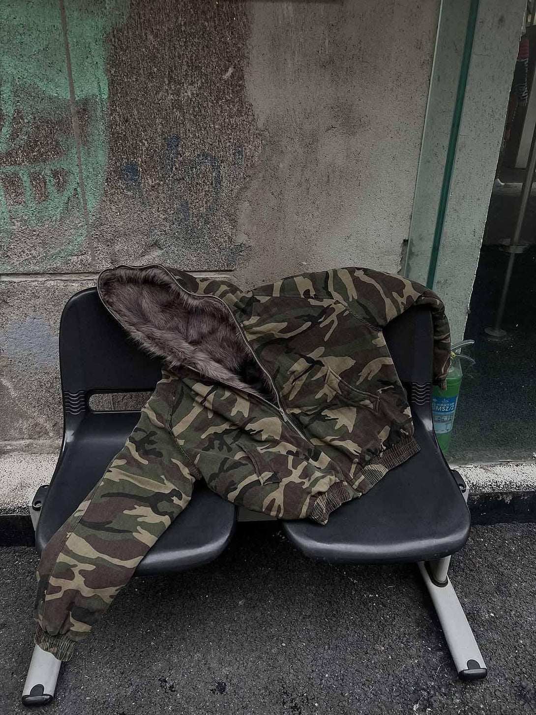 A camouflage hooded jacket with fur collar by TALISHKO, casually draped on a seat.