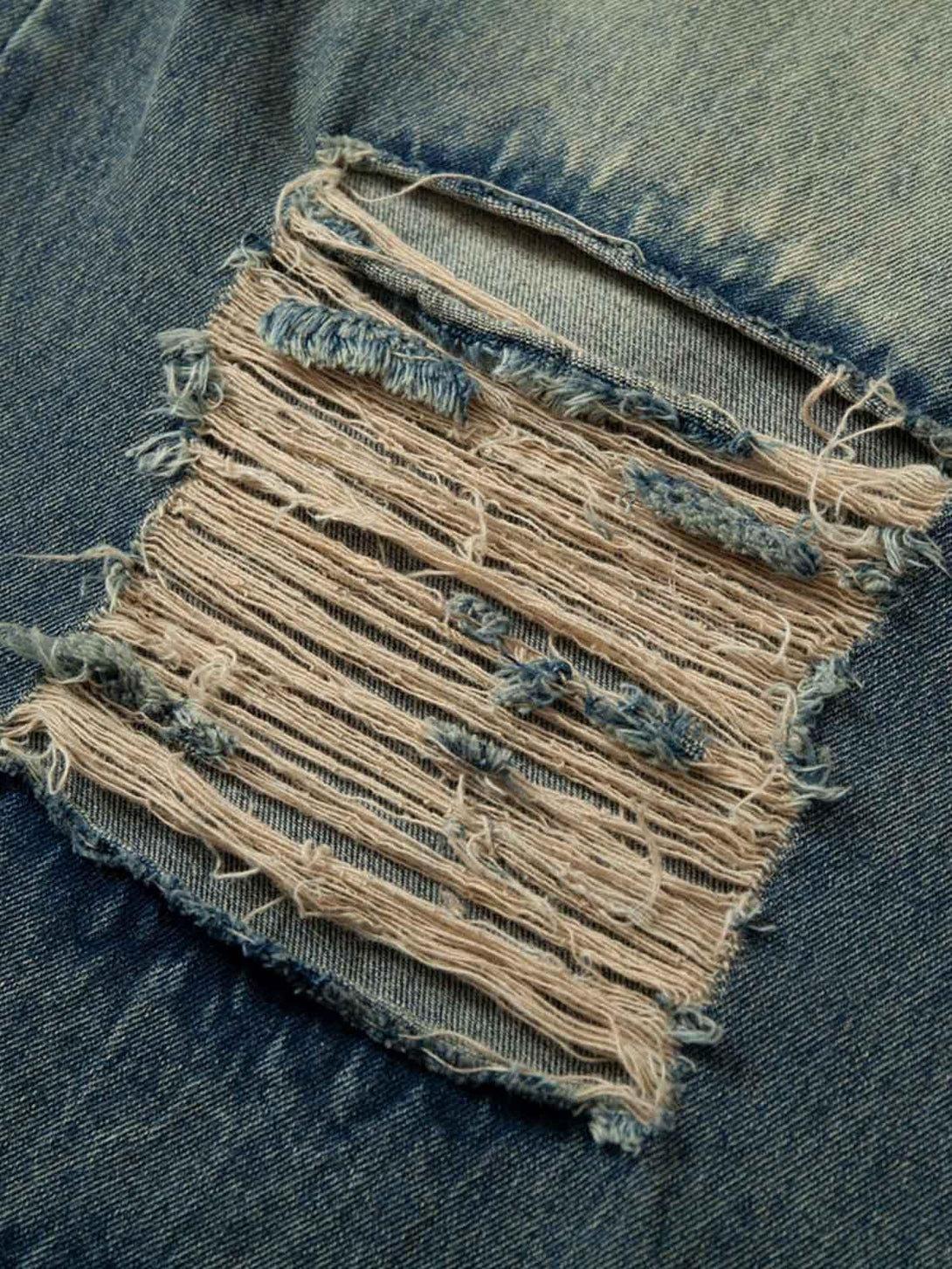 Focusing on TALISHKO jeans' distressed patchwork detail, highlighting rugged denim texture.