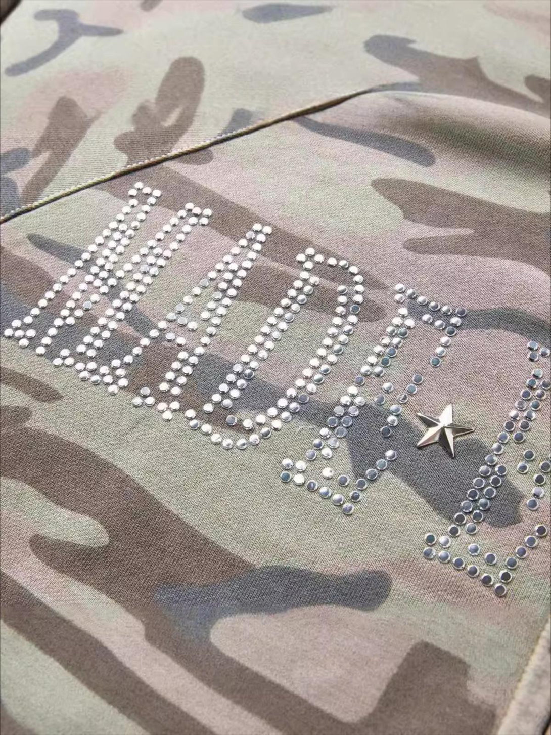 A detailed view of the TALISHKO camouflage hoodie with sparkling sequin lettering and star embellishment.