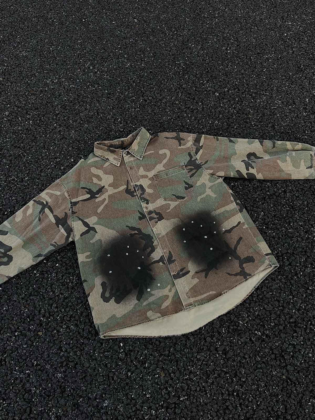 A camouflage denim shirt by TALISHKO with a unique distressed pattern, laid on a textured surface.