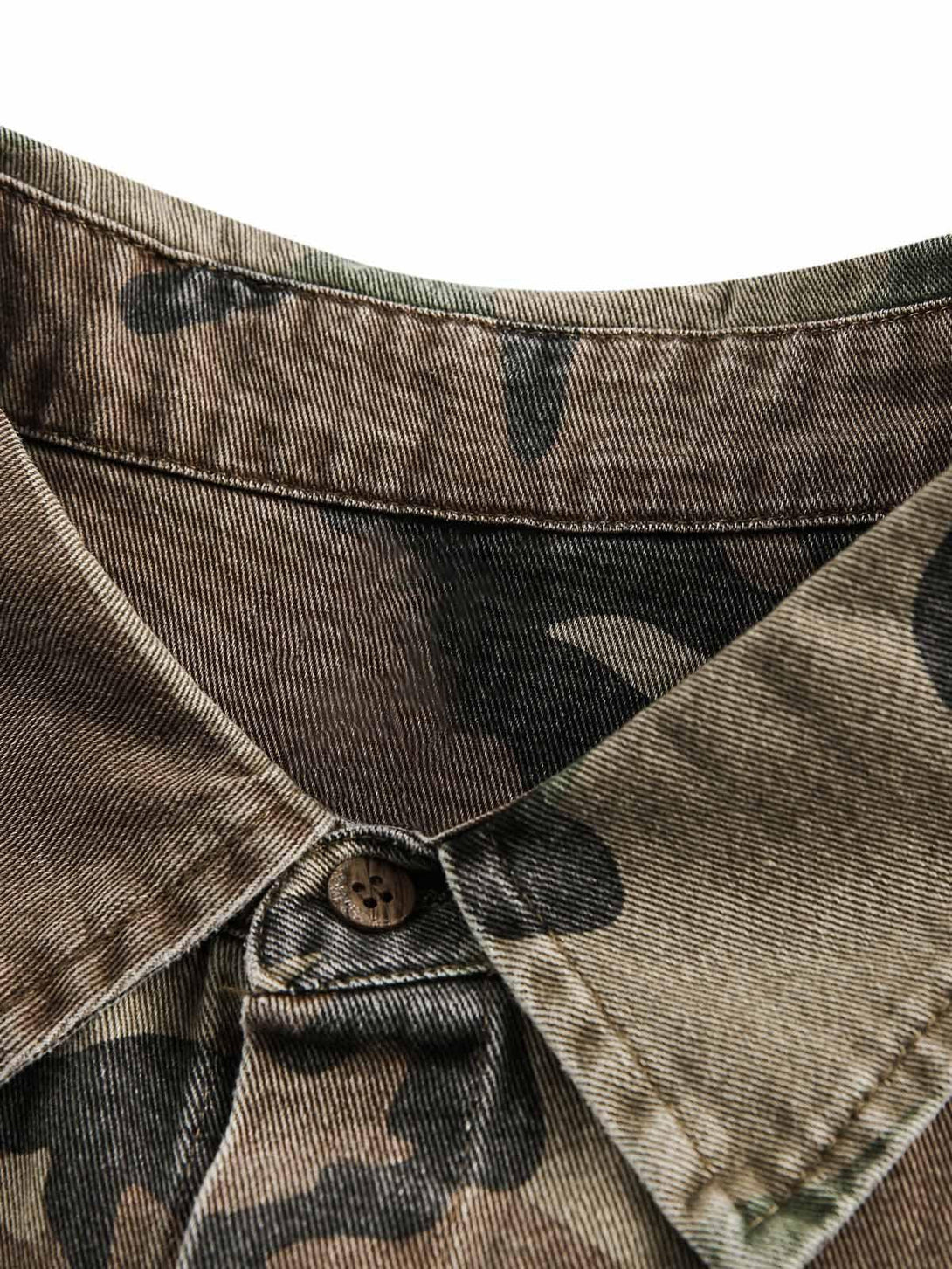 A detailed view of the camouflage pattern and button on a TALISHKO distressed denim shirt.