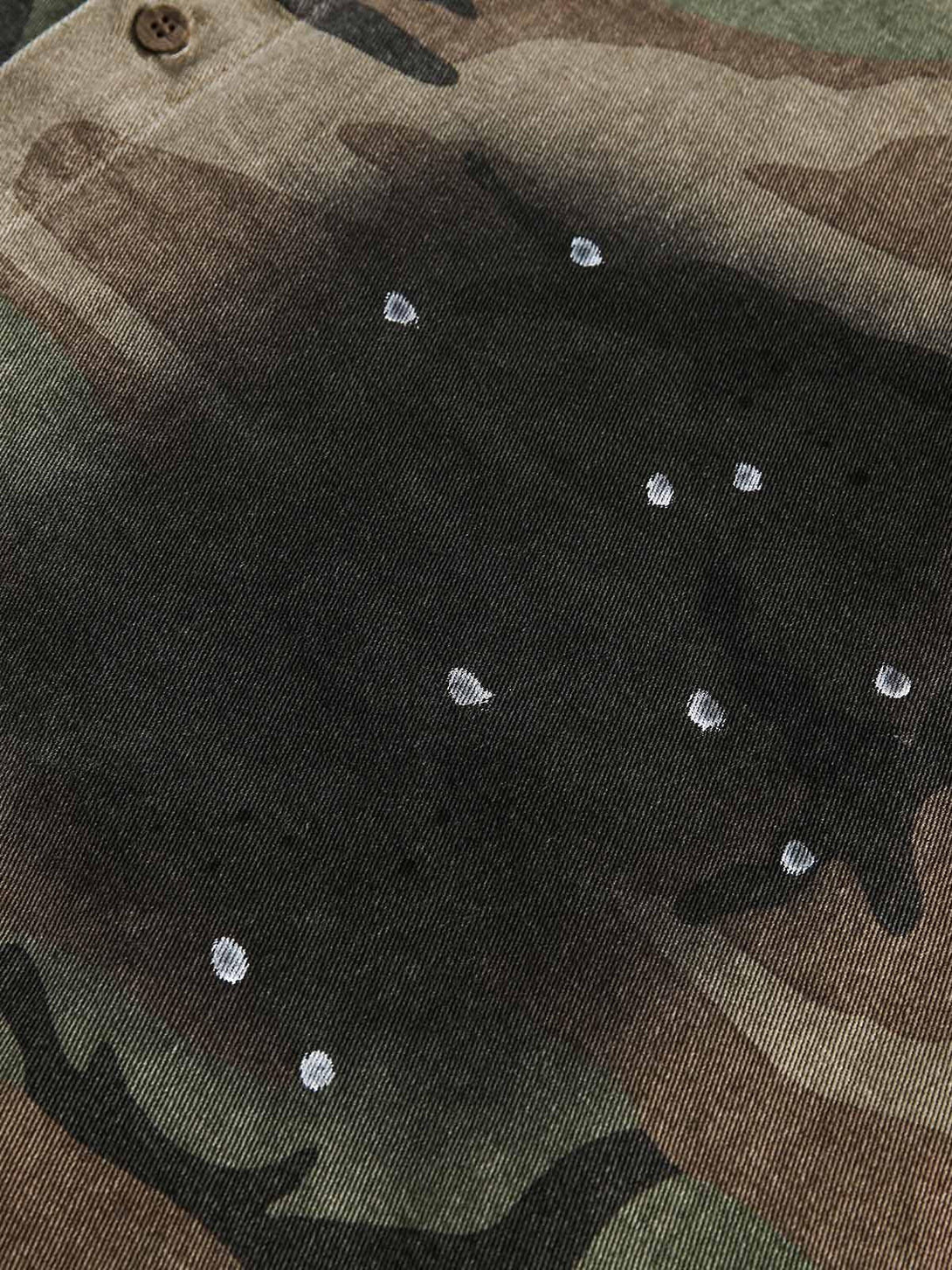 A close-up of the camouflage fabric and button detail on a TALISHKO distressed denim shirt.