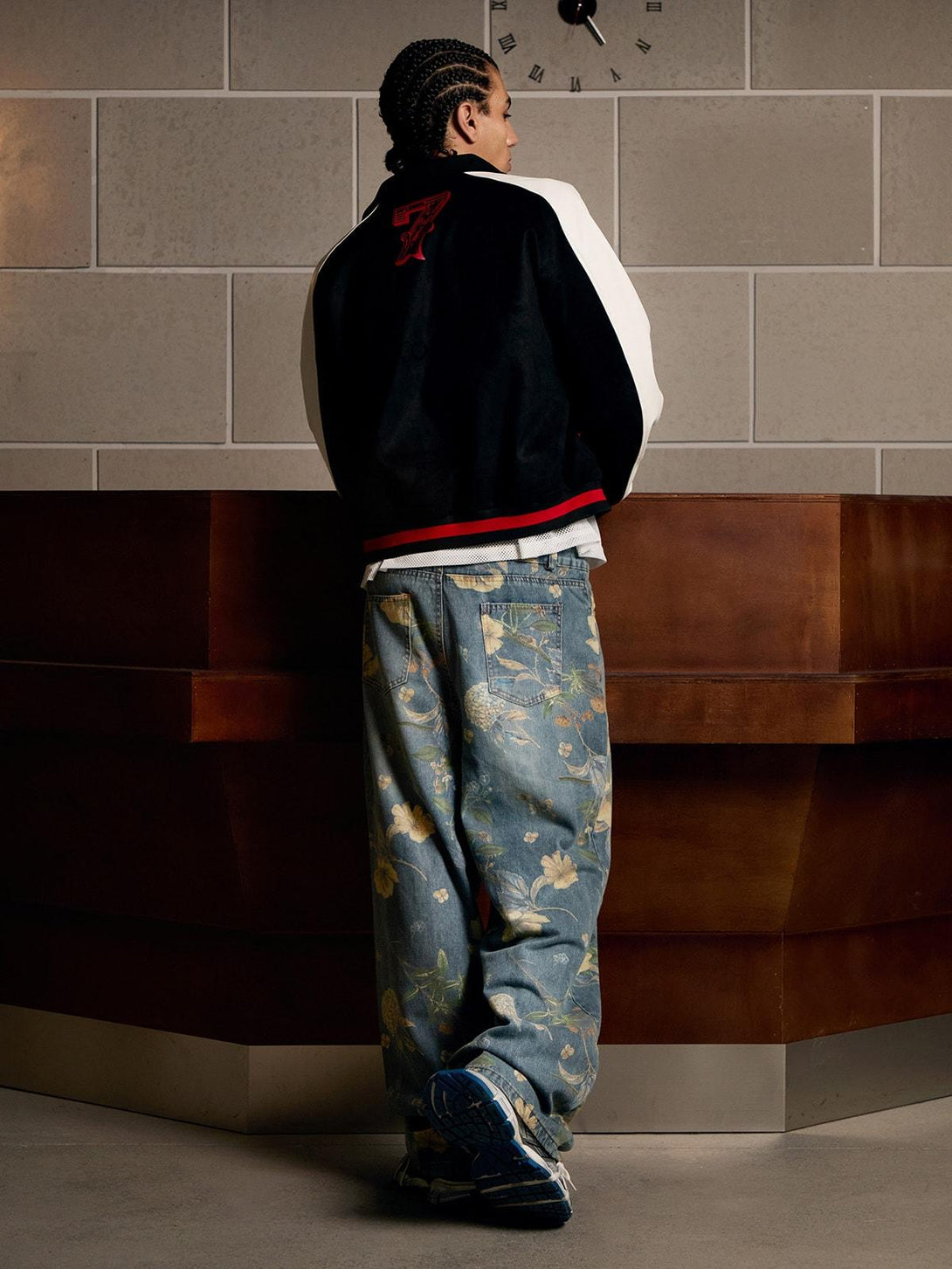 Model in floral carpenter pants by TALISHKO, styled with a varsity jacket and sneakers.