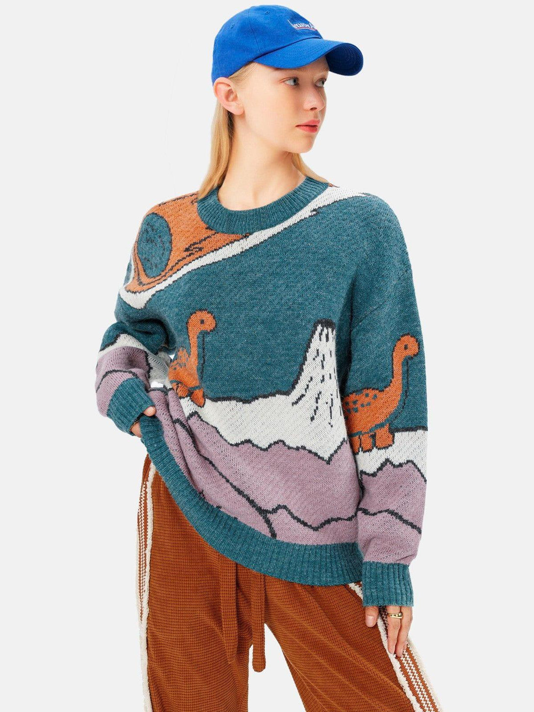 Model wearing a TALISHKO dinosaur knit sweater with playful cartoon design, paired with a blue cap.