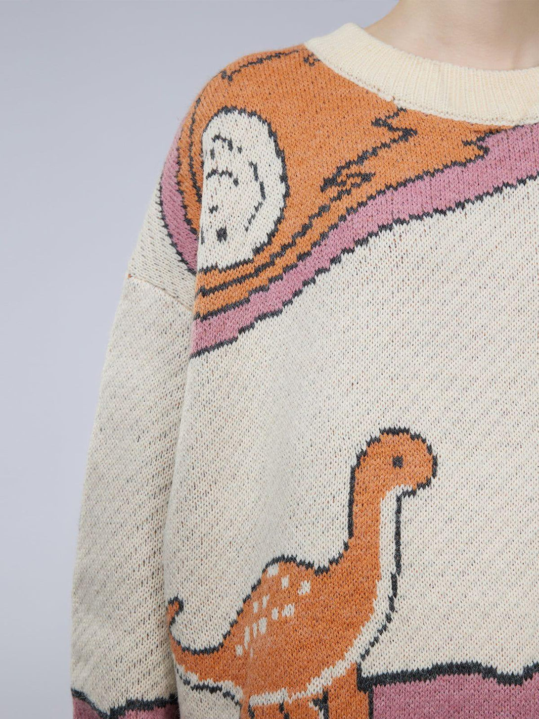 Close-up of a whimsical dinosaur pattern on a knit sweater by TALISHKO, showcasing playful design.