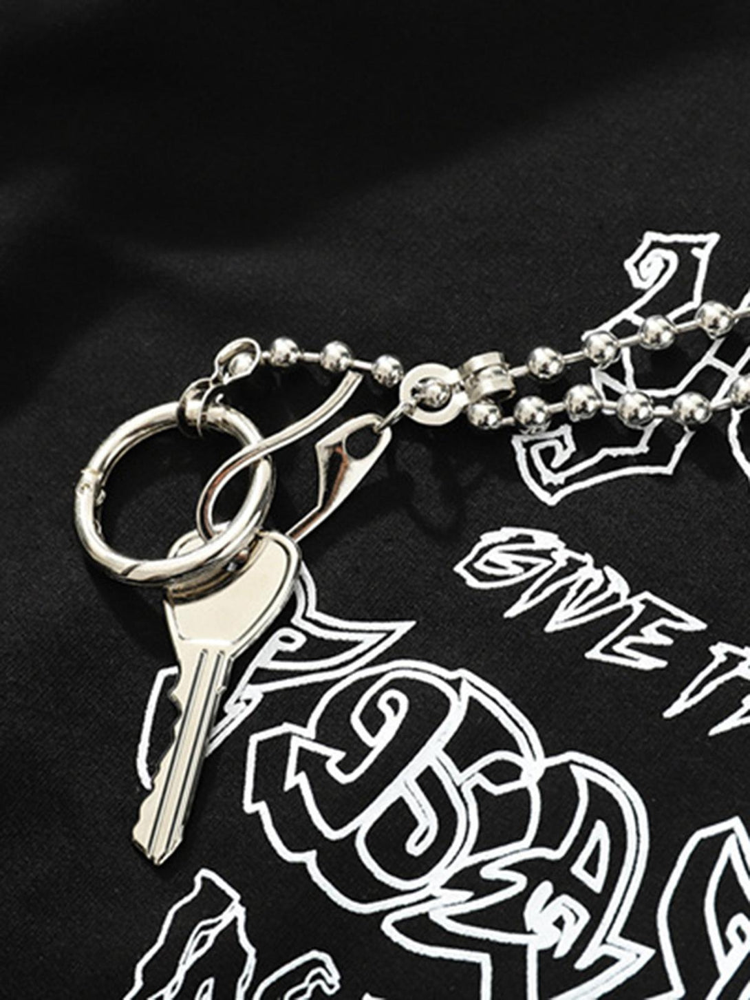 A close-up of TALISHKO's chain detail against black fabric, highlighting graphic design elements.