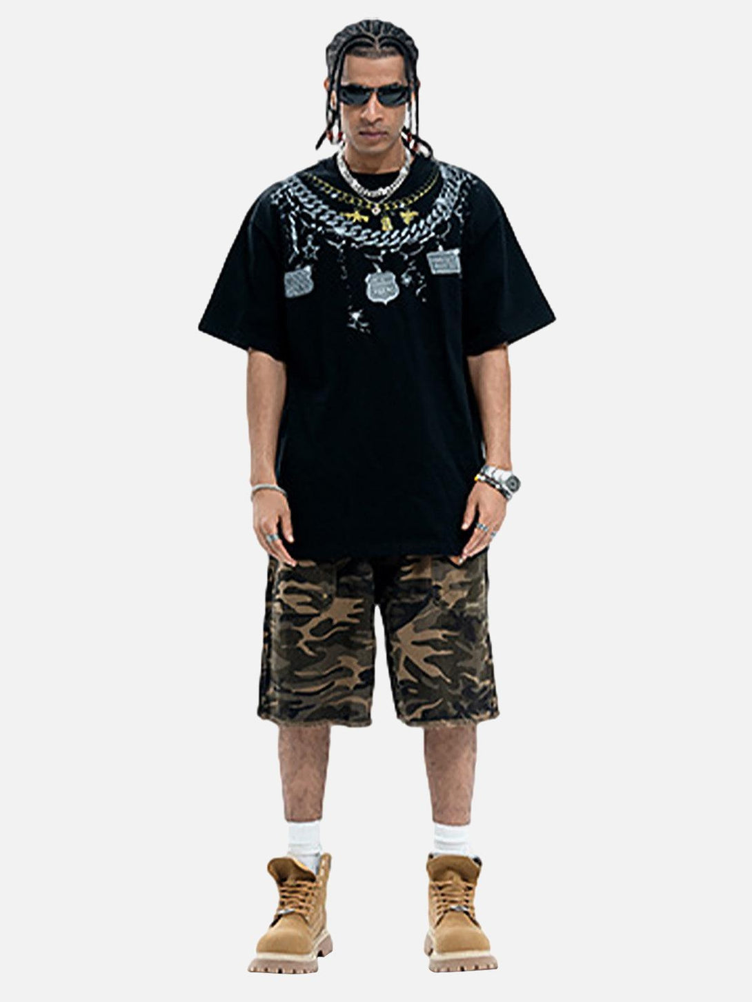 Model in a TALISHKO chain print T-shirt, paired with camo shorts and tan boots, exuding street style.