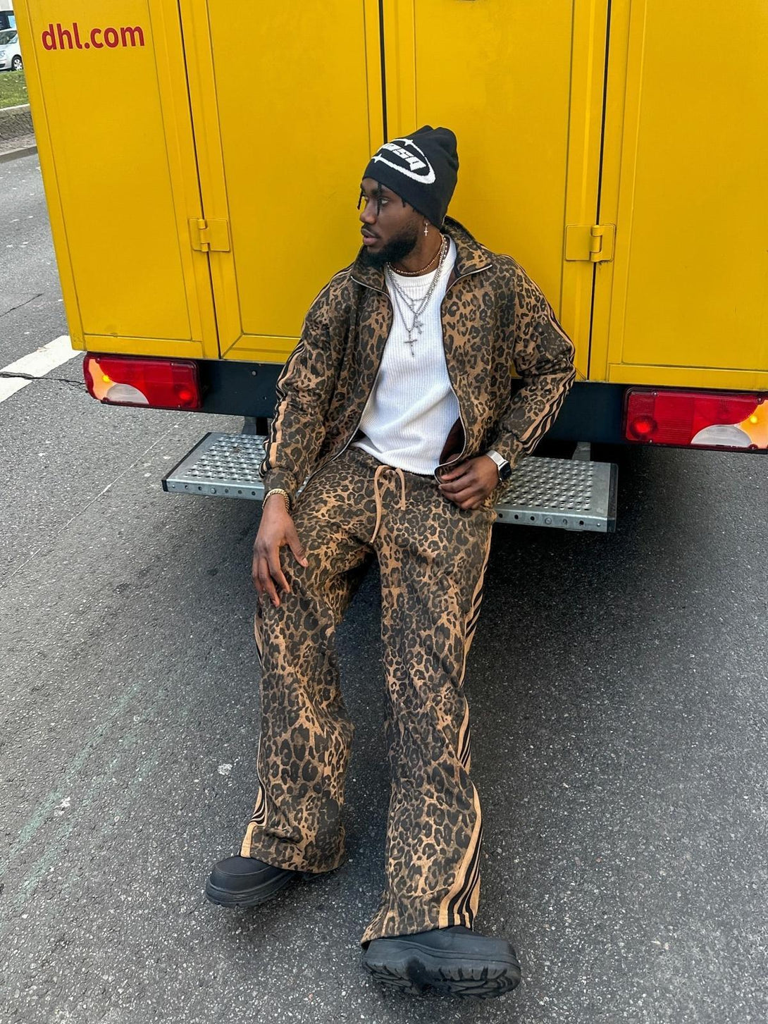 Model sitting on a step wearing TALISHKO cheetah print suede tracksuit, paired with a black beanie.