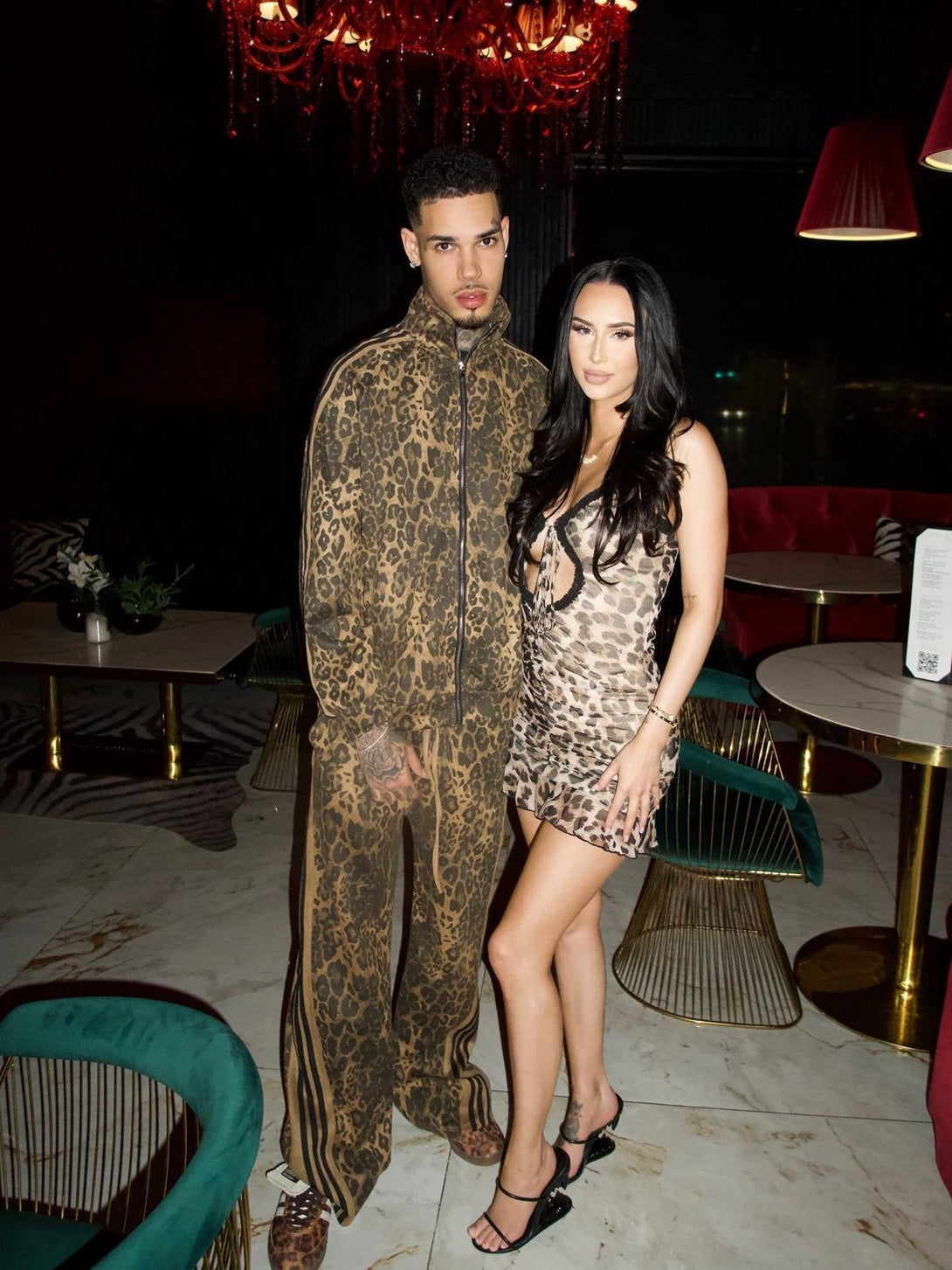Model in TALISHKO cheetah print tracksuit, paired with a stylish dress in a chic setting.