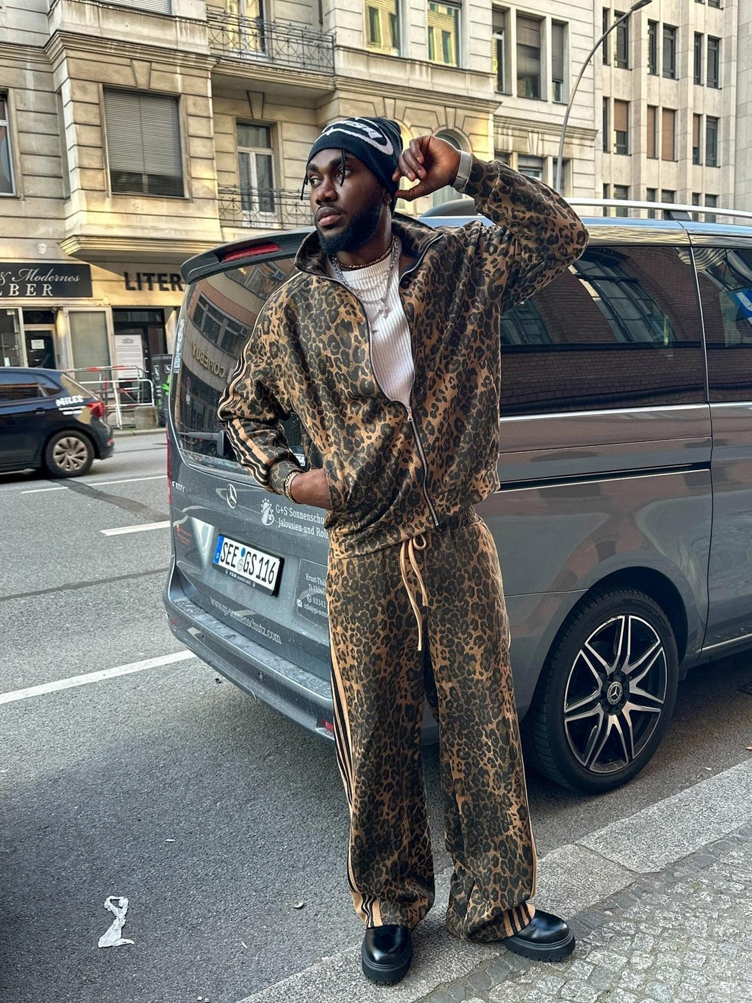 Model in a cheetah print suede track jacket and pants by TALISHKO, standing on the street.