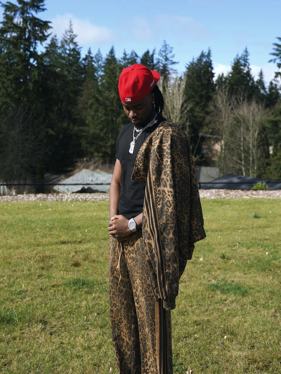 Model in a cheetah print track jacket and pants by TALISHKO, set against a forest backdrop.