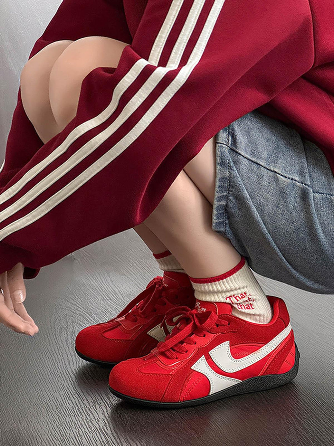 TALISHKO red suede low-top sneakers with white accents, styled with a red-striped outfit.