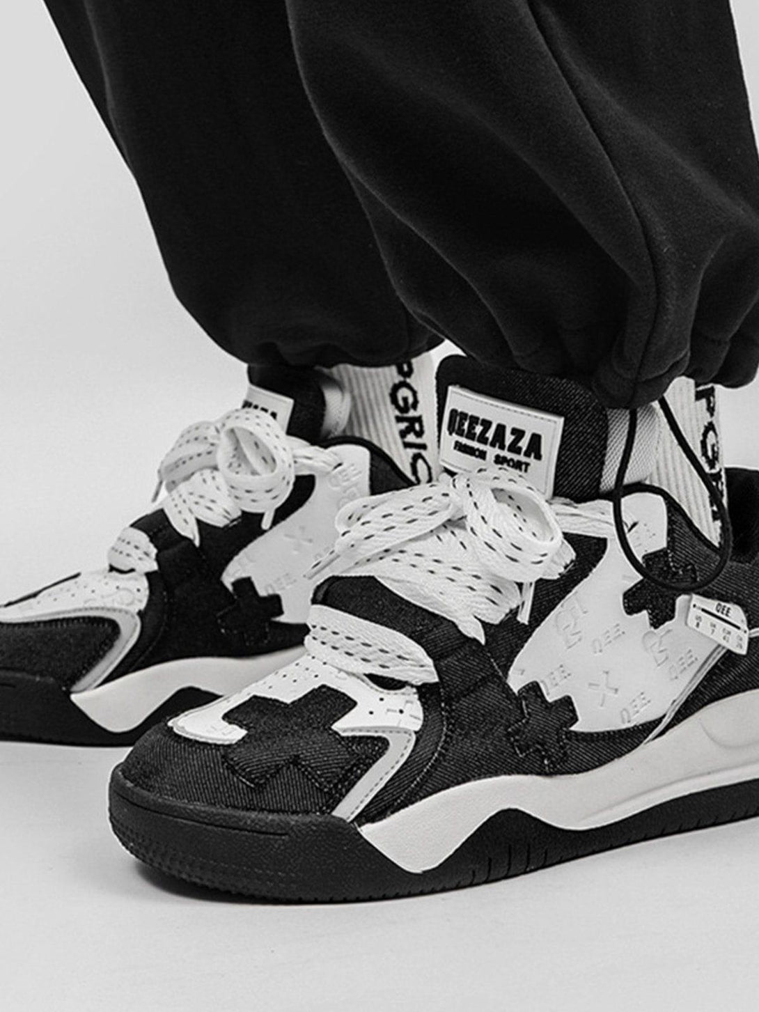 Model wearing black and white TALISHKO skate shoes with cross detailing and thick soles.