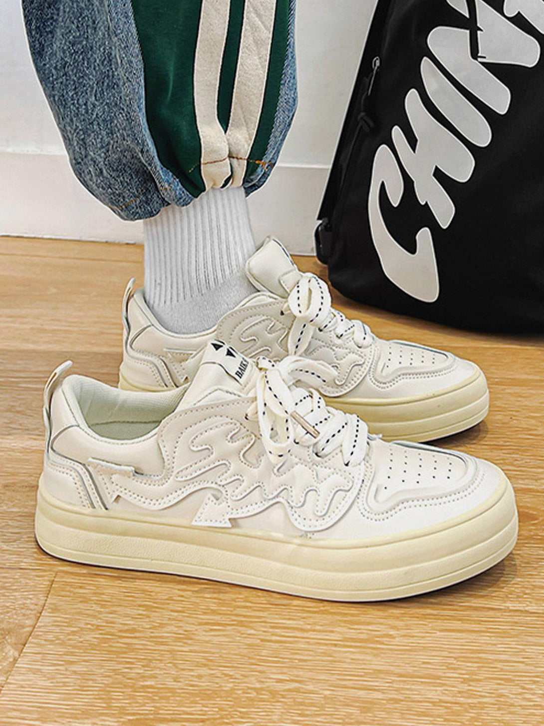 Model wearing TALISHKO white casual shoes with wavy patch detail, paired with sporty pants.