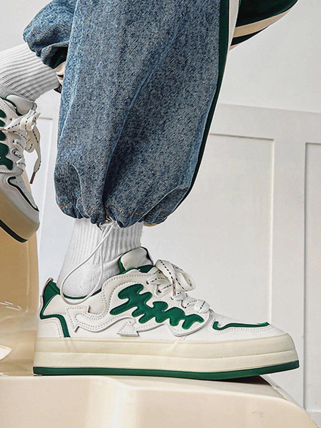 Model showcasing TALISHKO colorblock casual shoes with green accents, styled with denim joggers.
