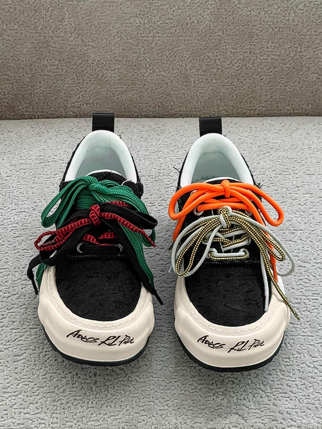 Front view of TALISHKO sneakers featuring mismatched colorful laces for a bold, playful look.