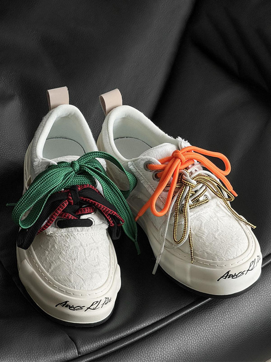 TALISHKO sneakers featuring mismatched colorful laces on a black leather background, front view.