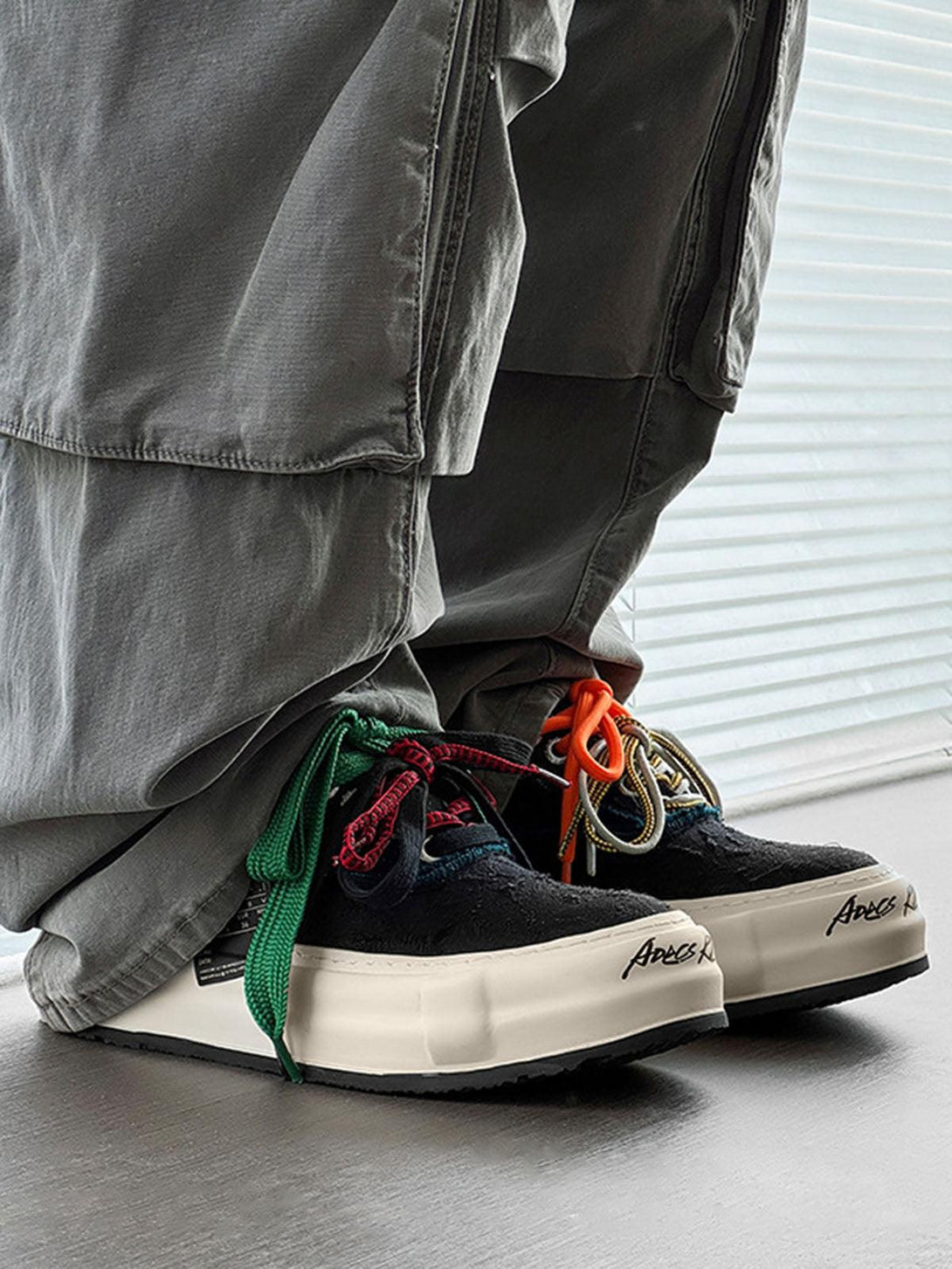 TALISHKO sneakers with colorful laces and thick soles, styled with casual gray pants.