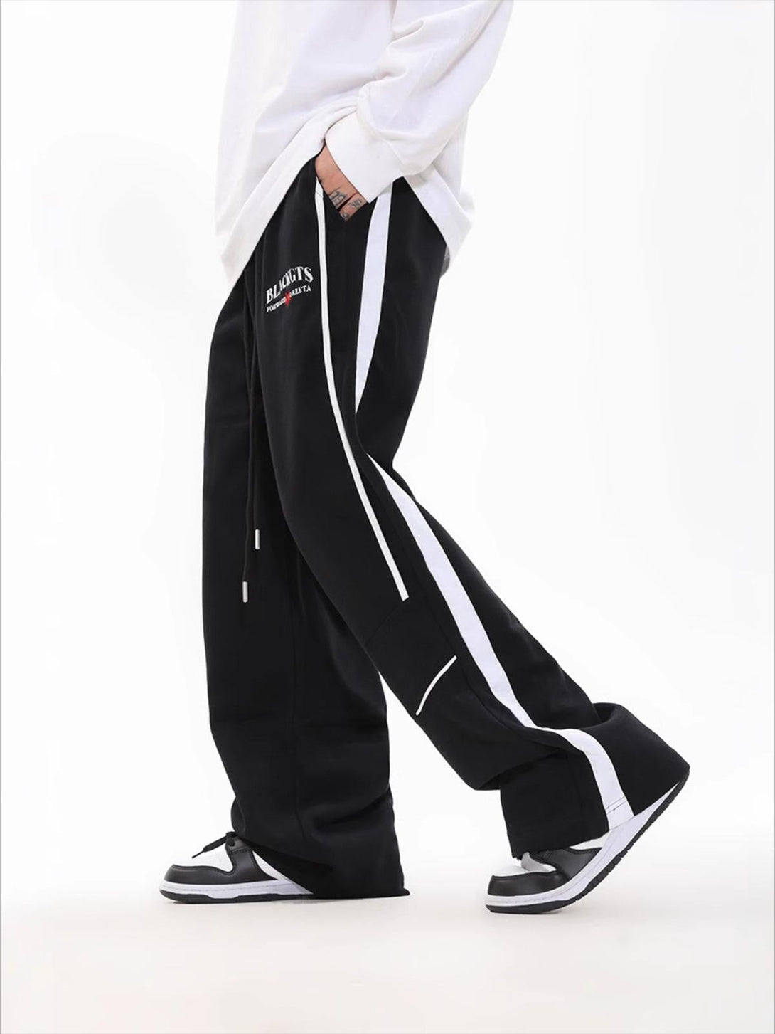 Model wearing black loose sweatpants with white contrast stripes by TALISHKO, paired with sneakers.