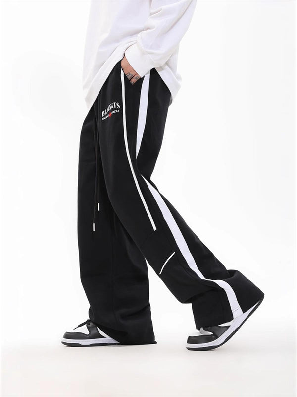 Model wearing black loose sweatpants with white contrast stripes by TALISHKO, paired with sneakers.