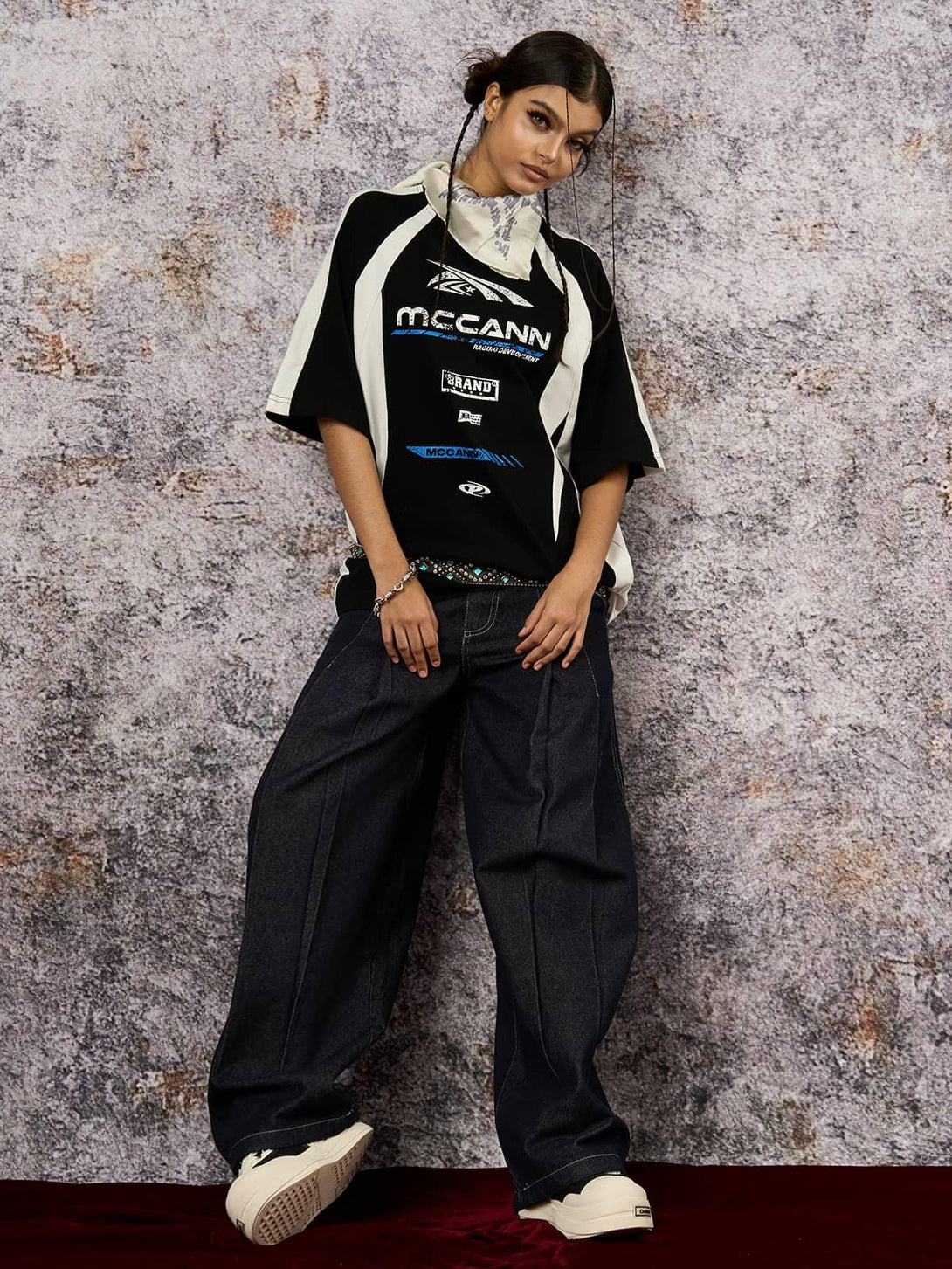 Model in a TALISHKO motorcycle print T-shirt paired with wide-leg jeans against a textured backdrop.
