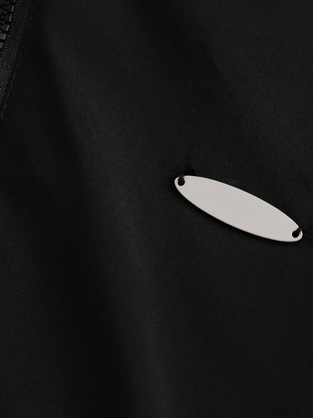 A close-up of the metal logo detail on a black track jacket by TALISHKO.