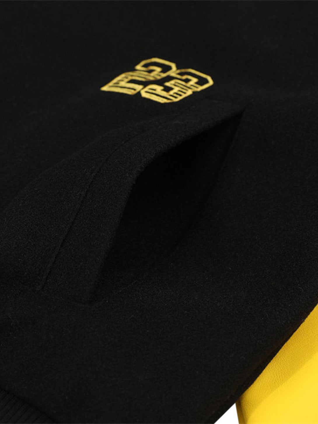 A detailed view of TALISHKO bomber jacket with bold yellow "23" embroidery on black fabric.