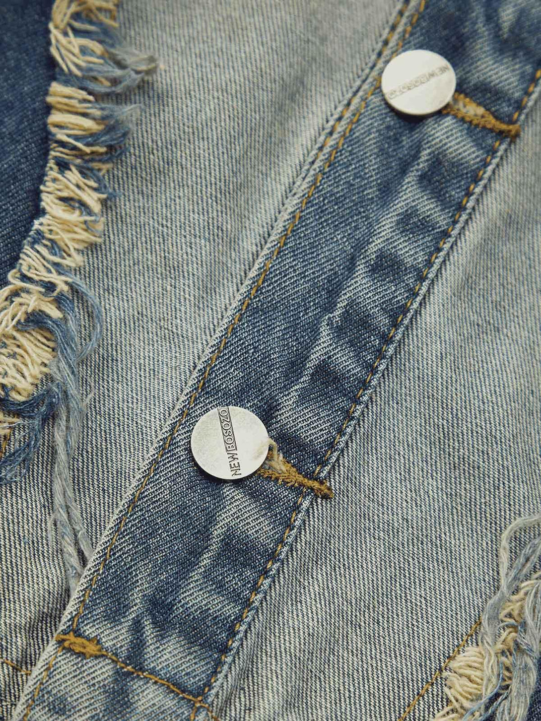 Intricate look at TALISHKO's denim vest, focusing on frayed edges and metal button detail.