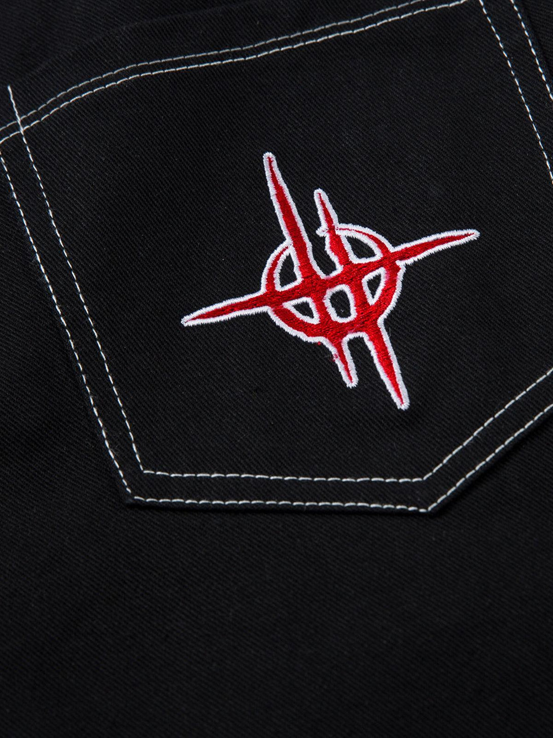 Focusing on the red flame embroidery on TALISHKO's black jeans, highlighting contrast stitching.