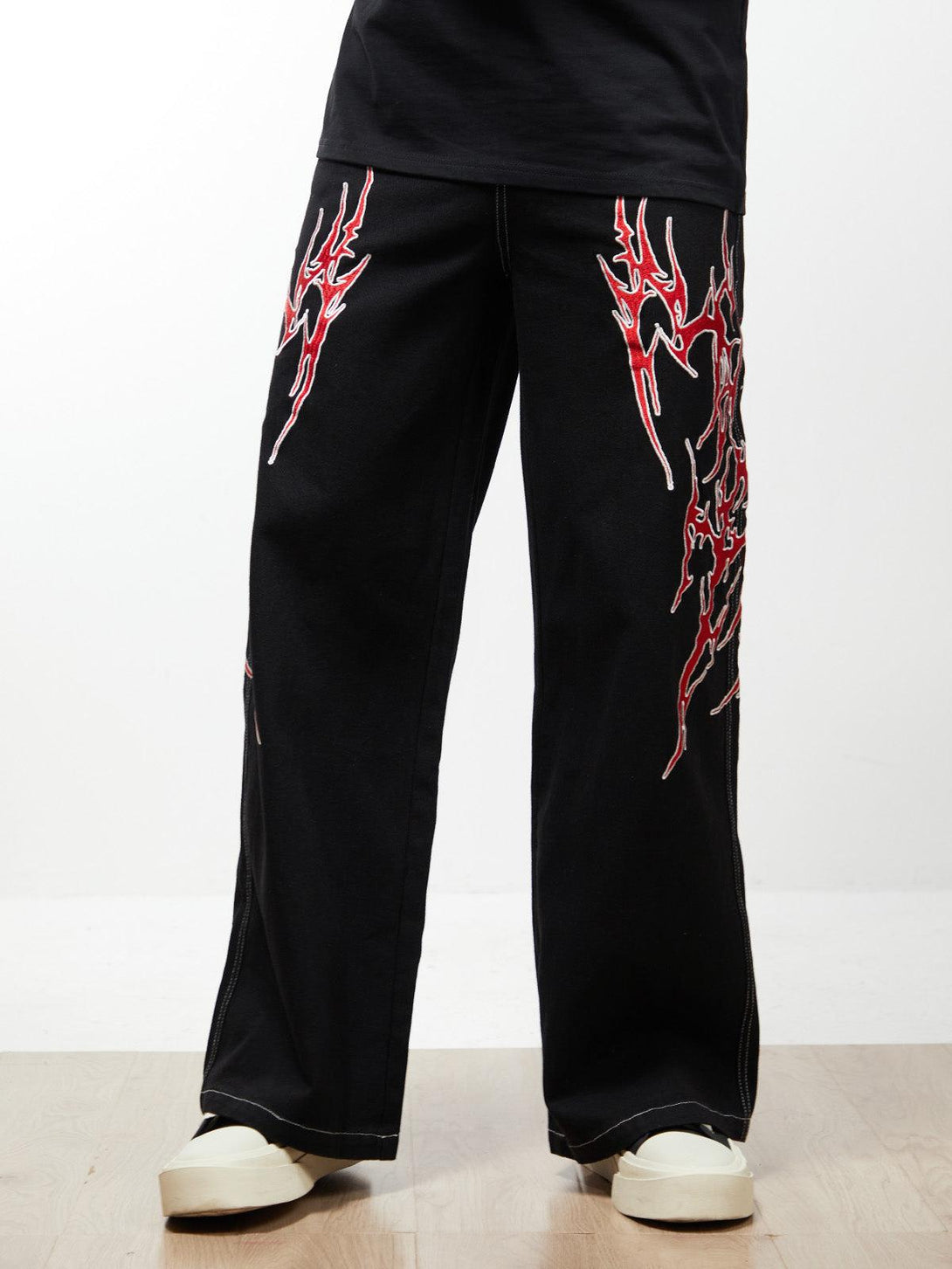 TALISHKO's black baggy jeans with striking red flame embroidery, worn with white shoes for a bold statement.