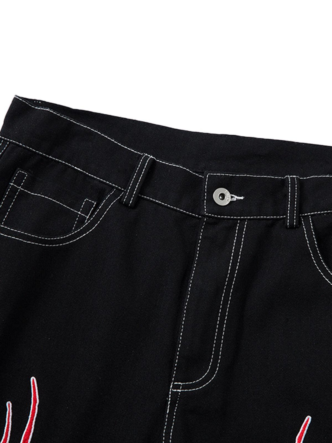 Detailed fabric and stitching of TALISHKO's black jeans, featuring bold red flame embroidery.