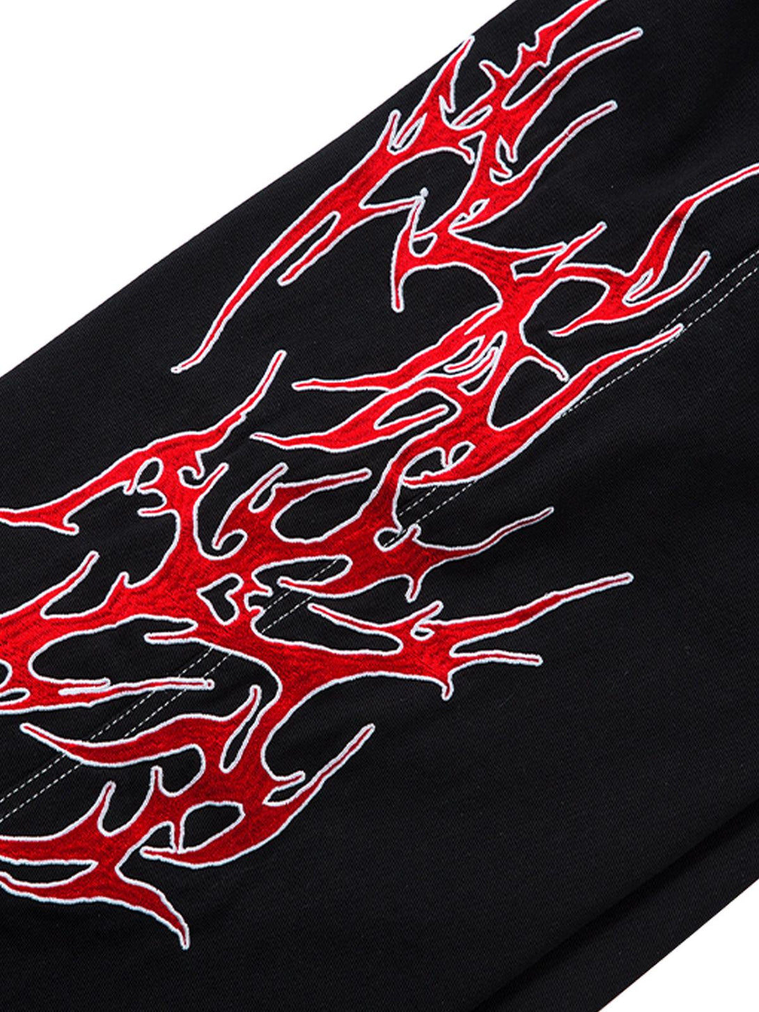 Intricate look at the red flame embroidery on TALISHKO's black baggy jeans, showcasing bold style.