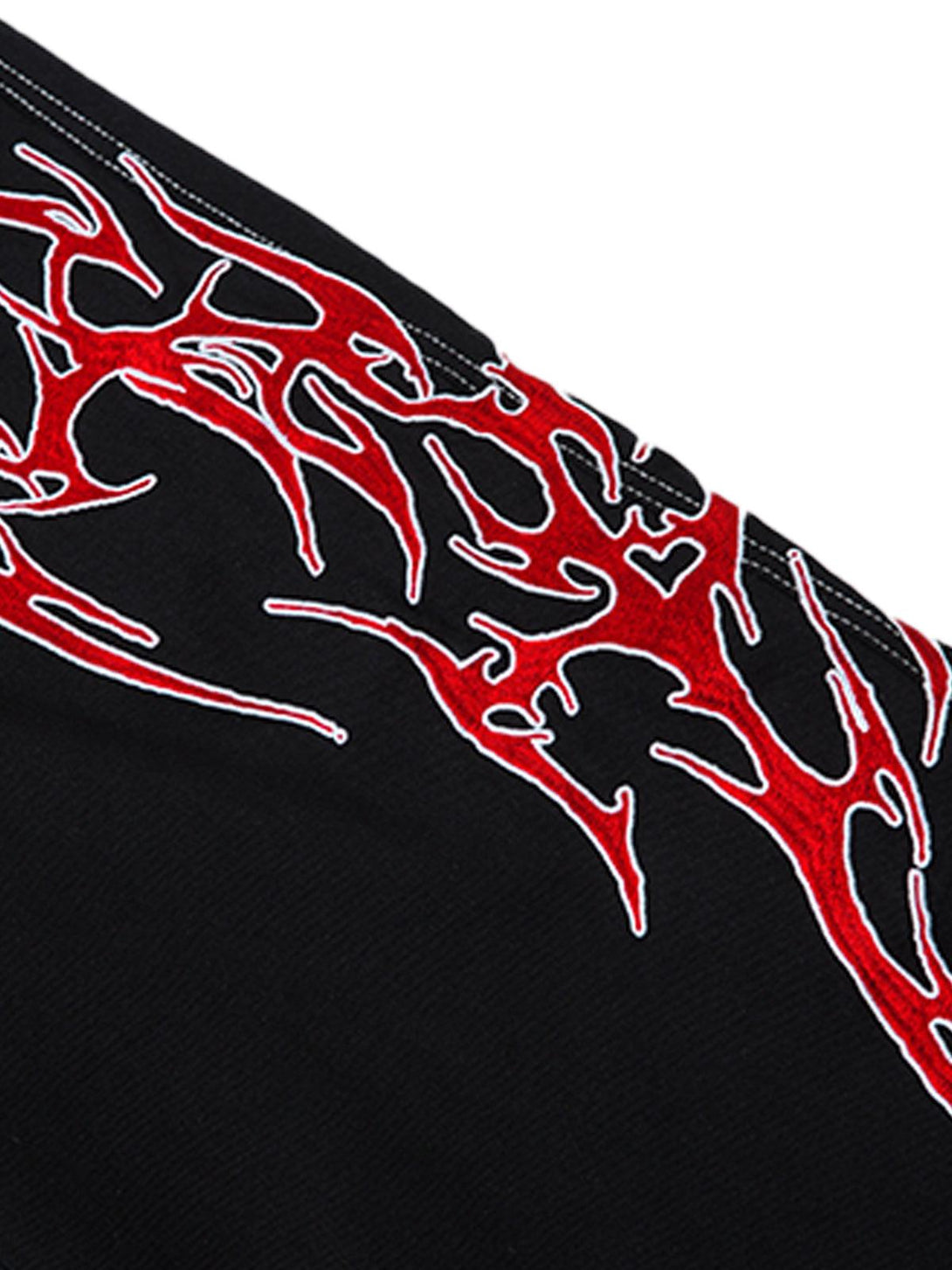 A tight crop highlighting the red flame embroidery on TALISHKO's black jeans, emphasizing bold style.