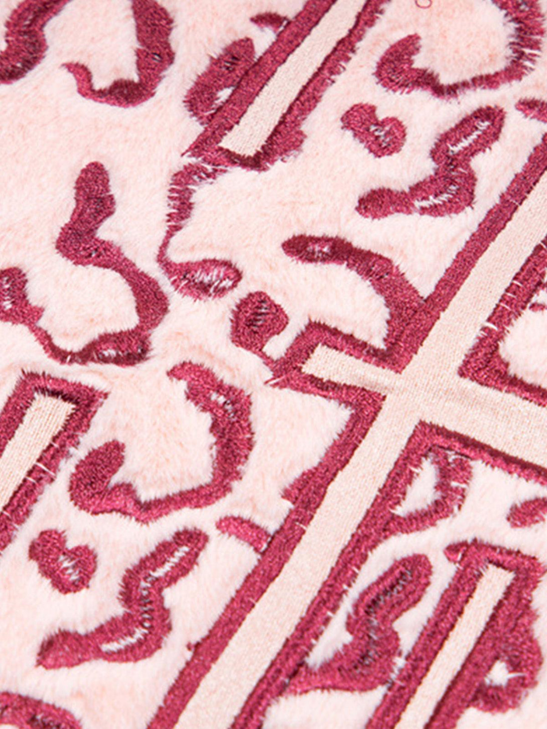 "Zoomed-in texture of pink TALISHKO T-shirt showing intricate cross and wave patterns."