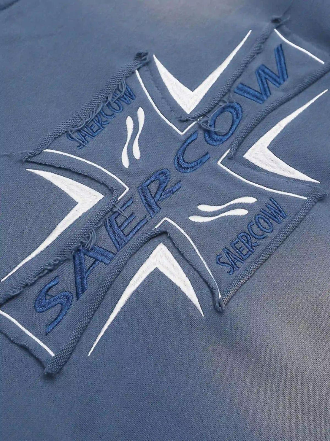 Intricate look at cross lettering embroidery on a blue washed hoodie by TALISHKO.