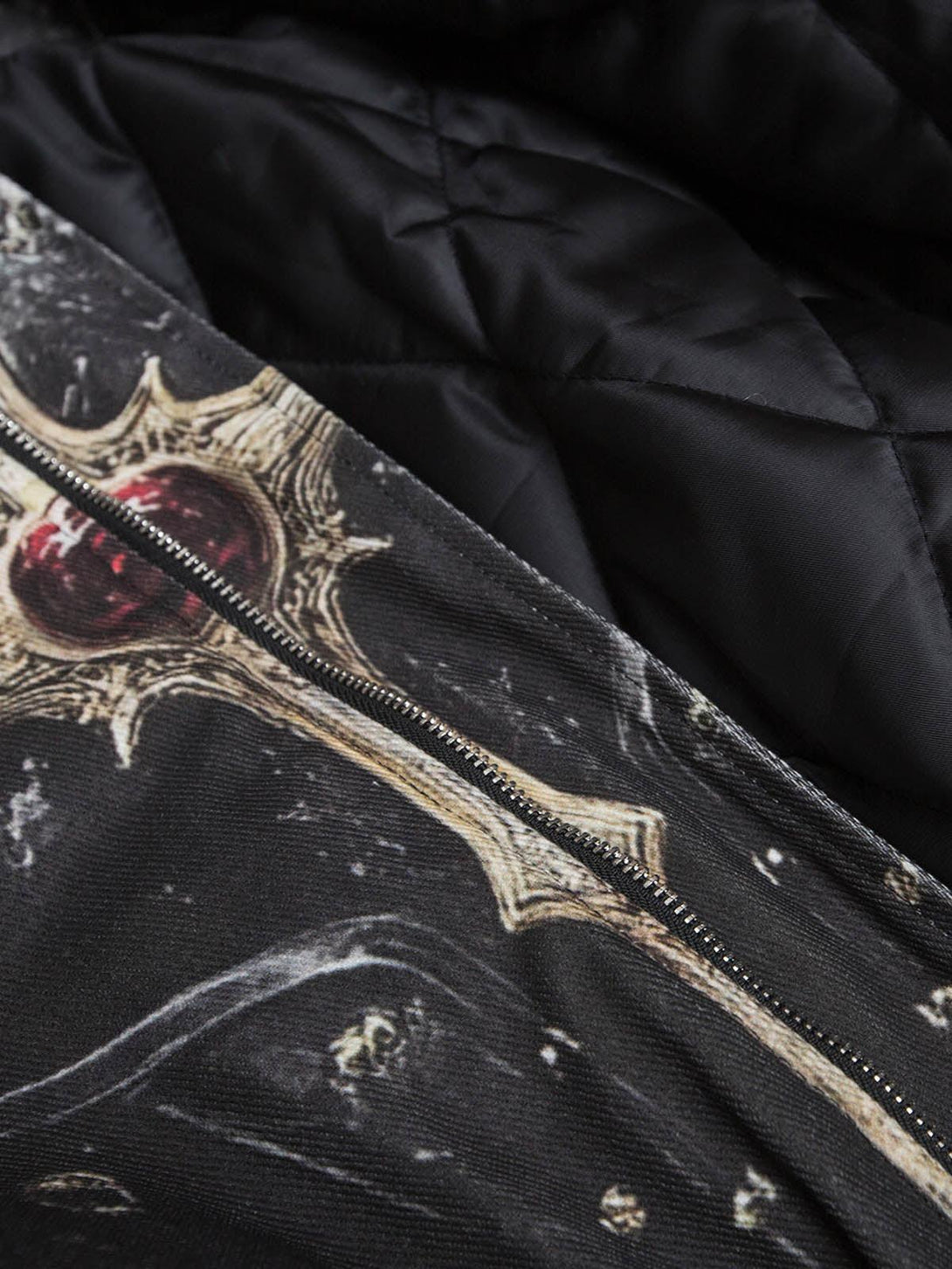 Detailed fabric and stitching on a TALISHKO quilted bomber jacket with a cross print design.