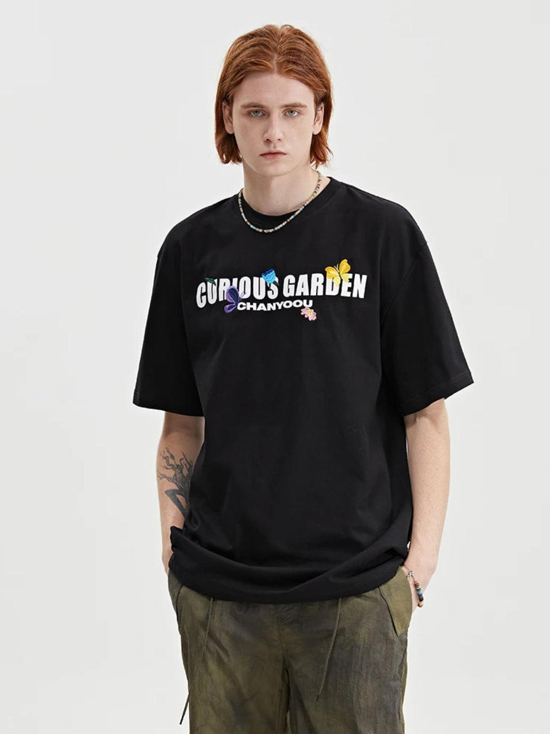 Model in a black TALISHKO tee with "Curious Garden" text and butterfly details on the front.