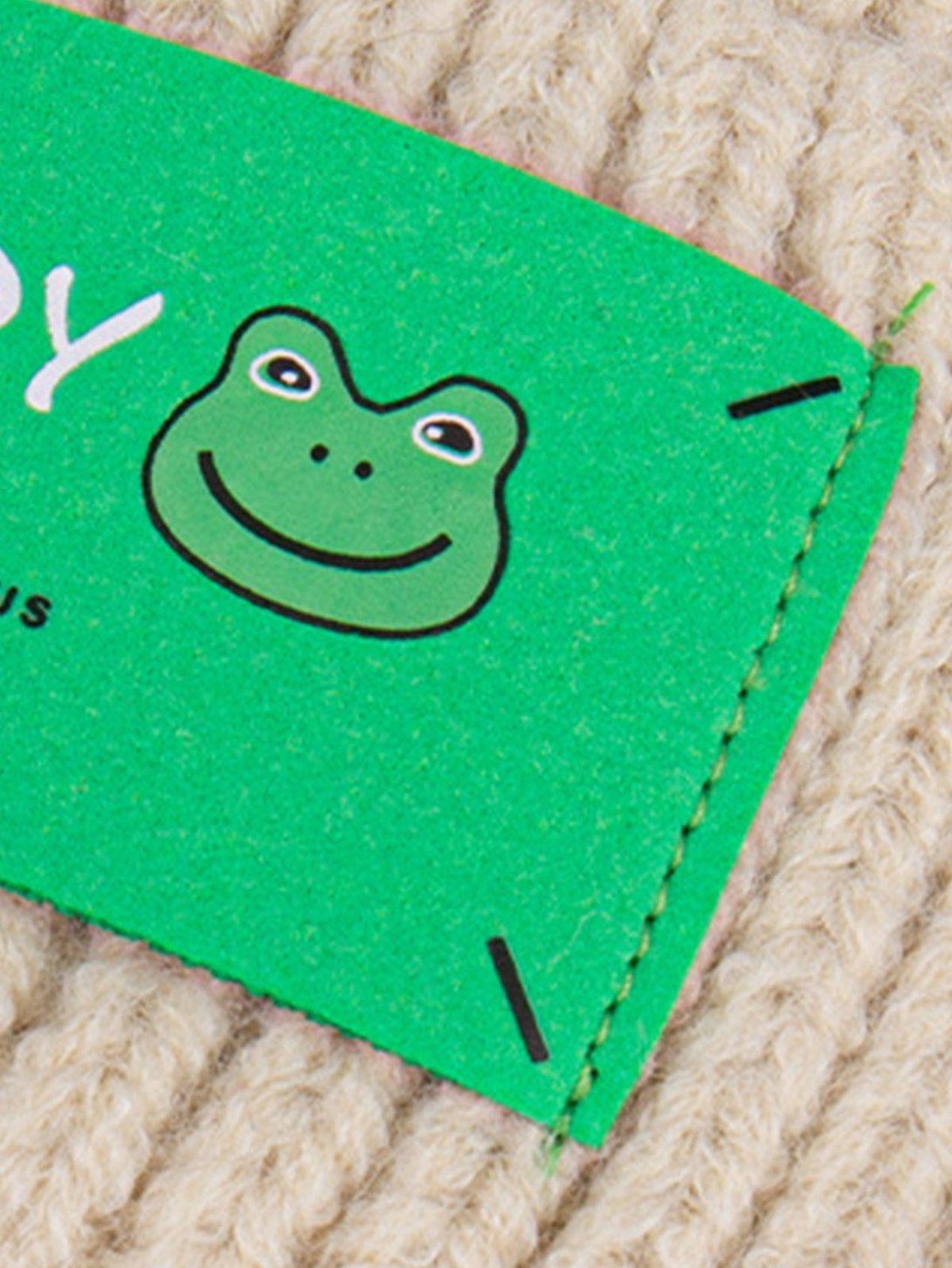 A close-up of TALISHKO's knit hat tag featuring a cute frog graphic, highlighting its playful design.