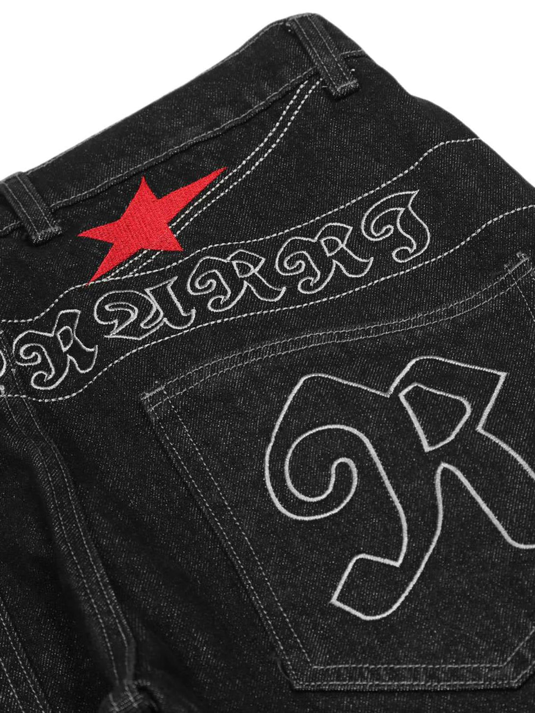 Detailed stitching and red star embroidery on TALISHKO's dark gothic jeans, highlighting style.