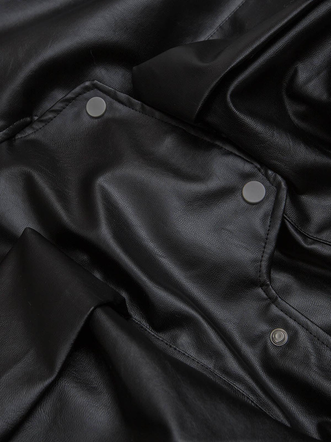 Intricate look at the black PU leather texture and snap details from a TALISHKO jacket.