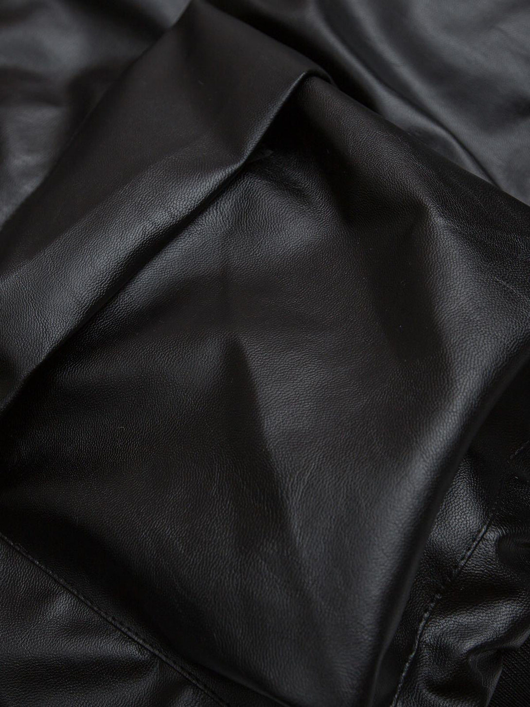 A zoomed-in texture of sleek black PU leather from a TALISHKO jacket, highlighting quality.