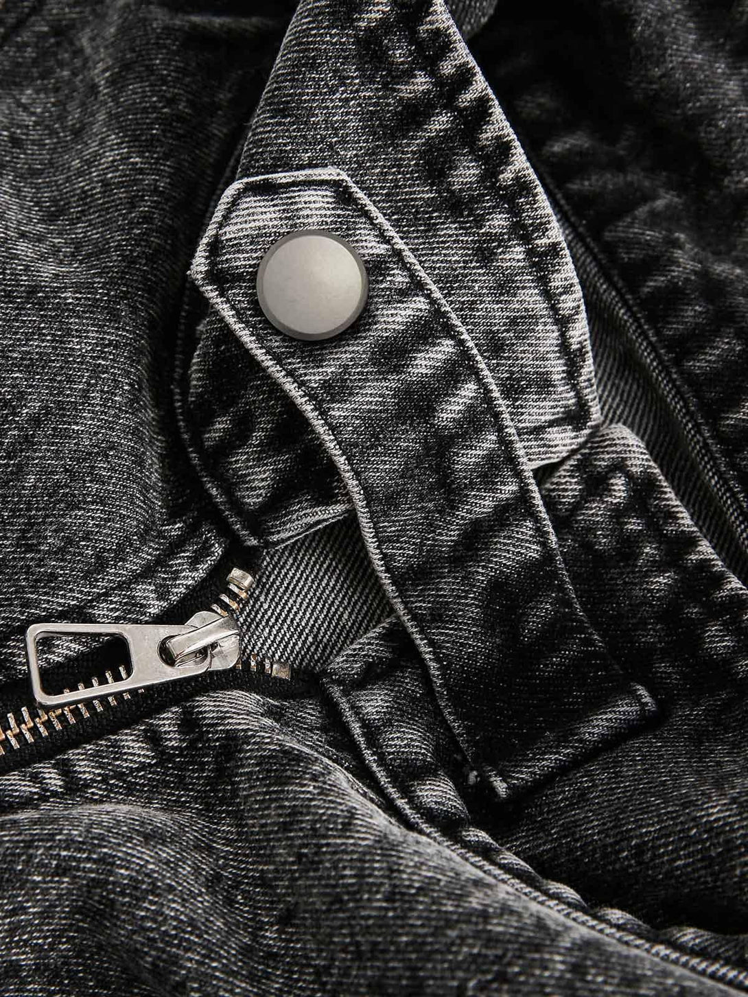 A detailed view of TALISHKO's denim jacket button and zipper, showcasing its deconstructed texture.