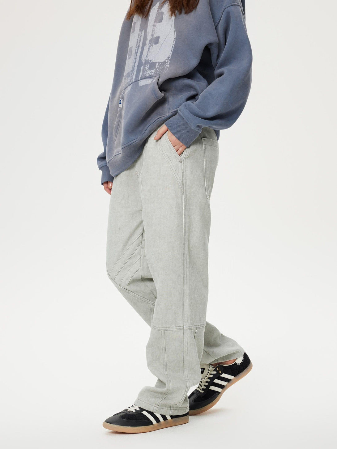 Model in gray TALISHKO patchwork jeans and blue hoodie with black sneakers, casual style.