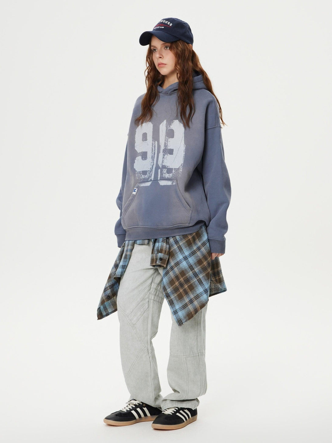 Model styled in TALISHKO patchwork jeans, layered with a plaid shirt and gray hoodie.