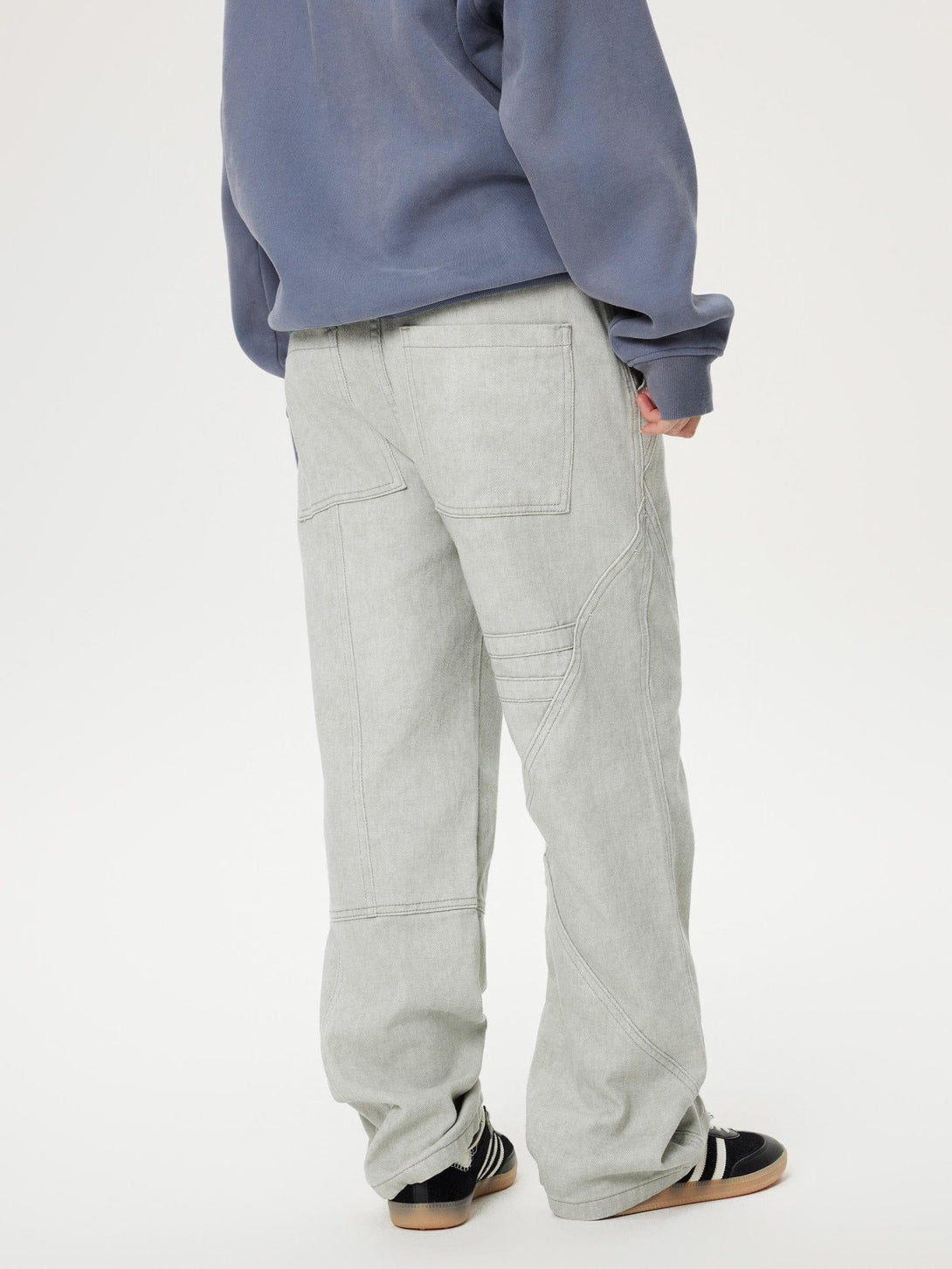 Rear view of TALISHKO deconstructive patchwork jeans paired with a blue hoodie and sneakers.